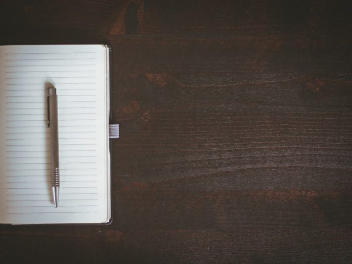 An open blank notebook with a pen on dark wood surface.