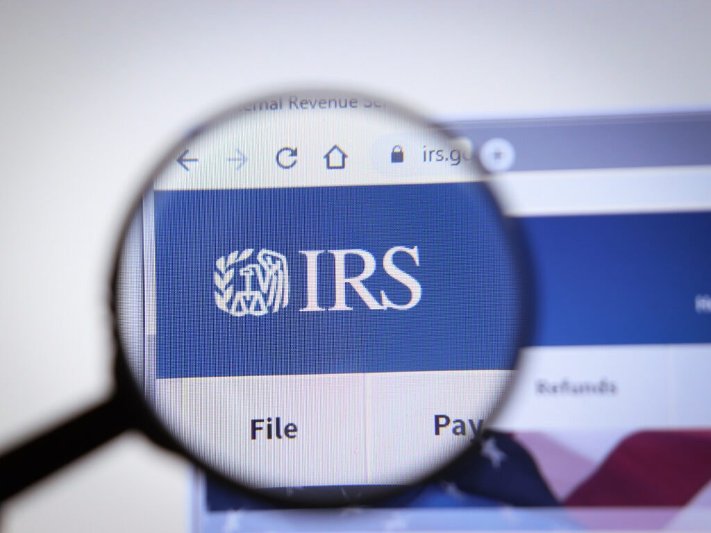 Website of the IRS (Internal Revenue Service) viewed through a magnifying glass, focusing on the logo.