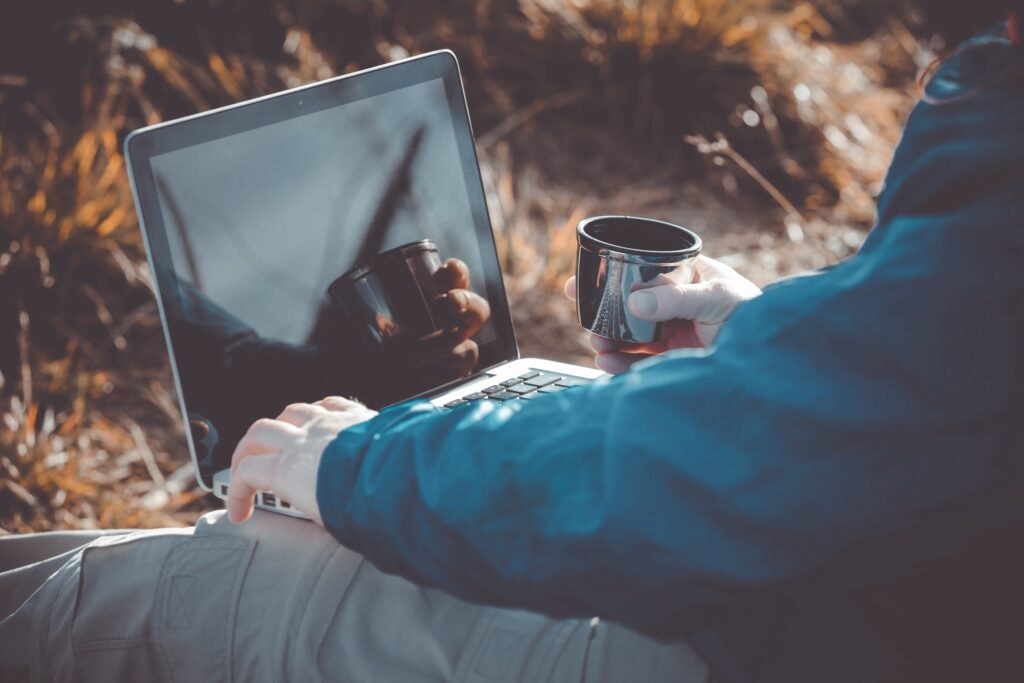 Person with a laptop in nature, holding a mug.