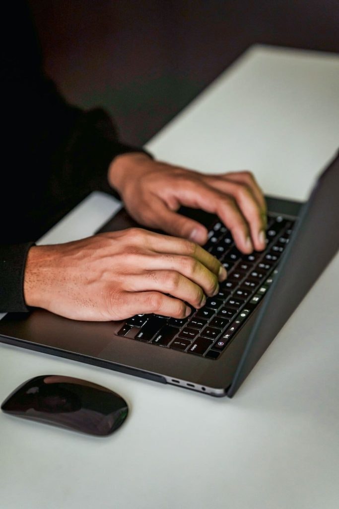 Person typing on a laptop with a black mouse on the table beside it.