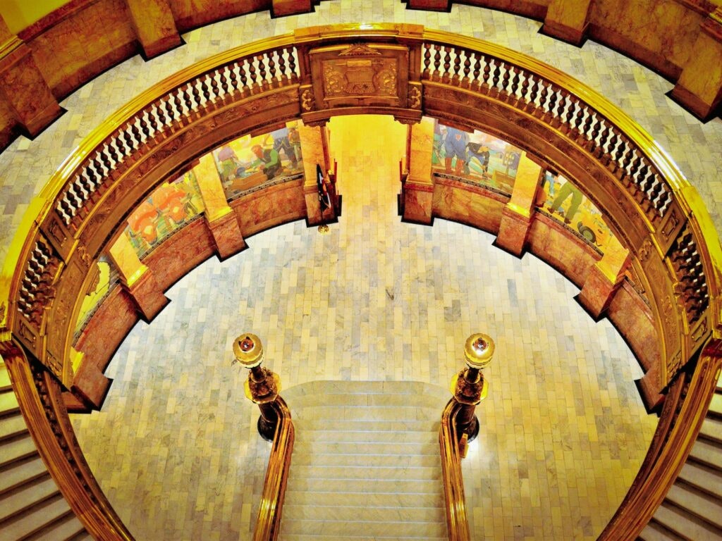 An opulent spiral staircase viewed from above, with intricate balustrades and warm lighting.