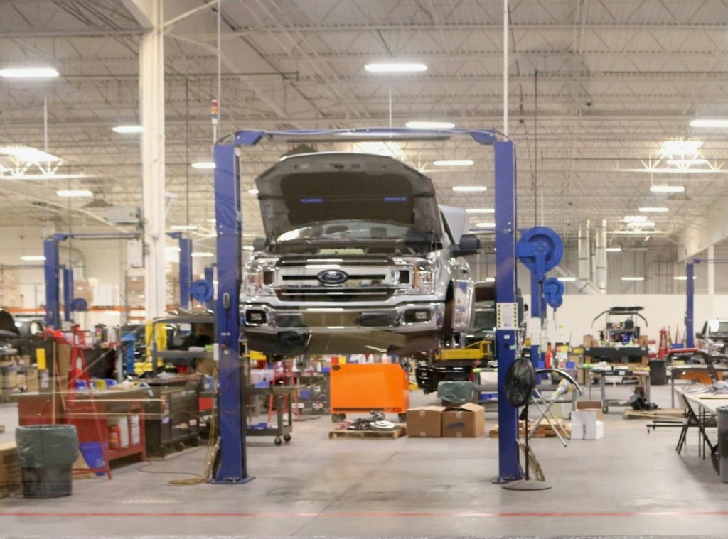 A truck on a hydraulic lift in a busy automotive workshop with tools and equipment around.