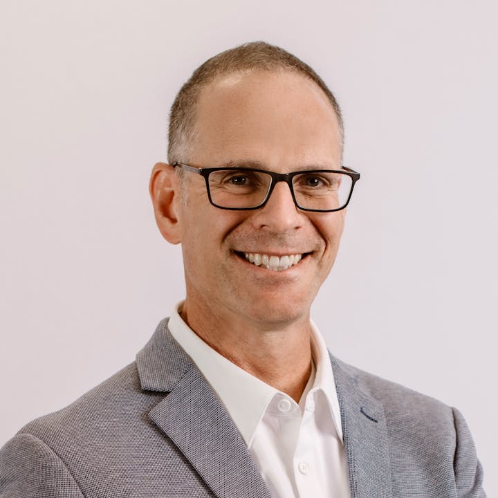 A man in a light gray suit and glasses smiles at the camera.