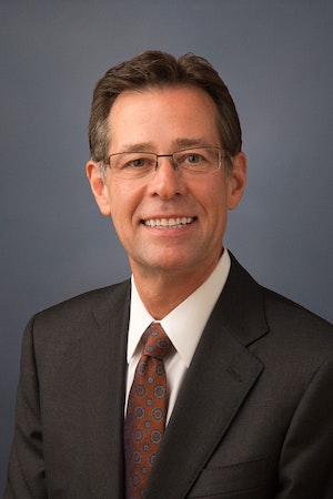 A smiling person in business attire with glasses against a blue background.