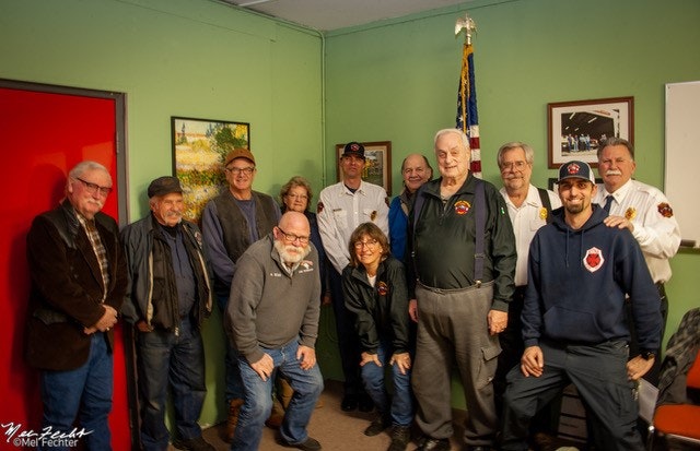 A group of people gathered in a room, likely a community meeting or event, with some wearing uniforms.