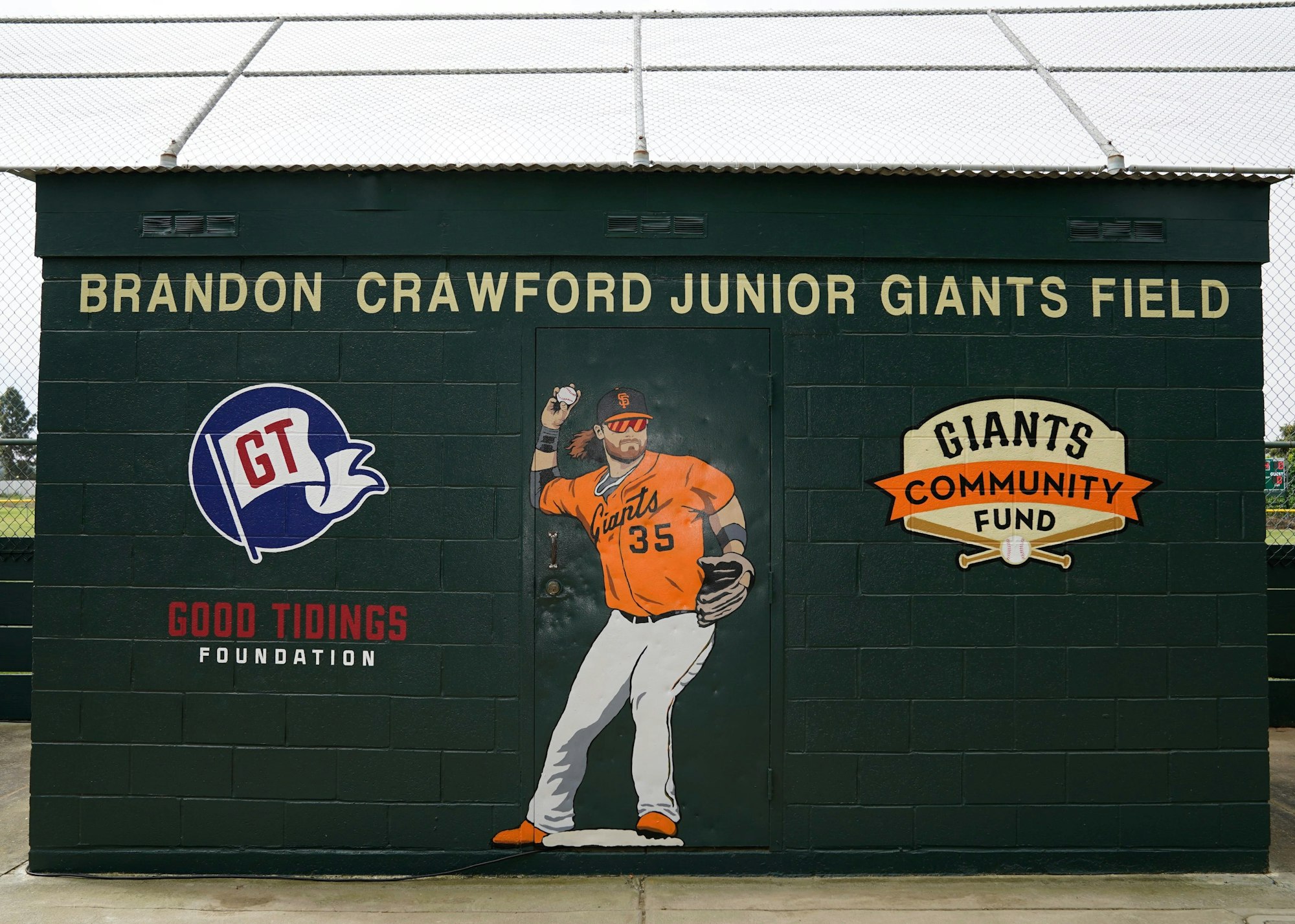 A mural of a baseball player and logos on a building at "BRANDON CRAWFORD JUNIOR GIANTS FIELD."