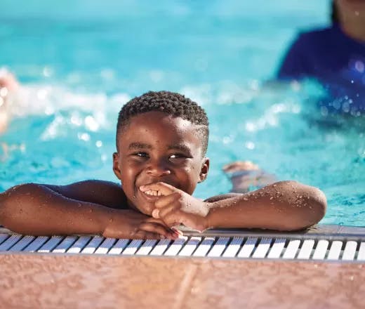 A smiling child resting on the edge of a swimming pool.