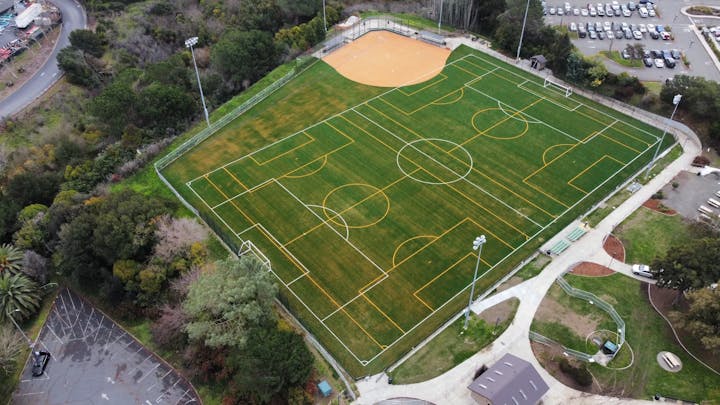 An aerial view of a sports complex with multiple soccer fields and a baseball diamond next to a parking lot.