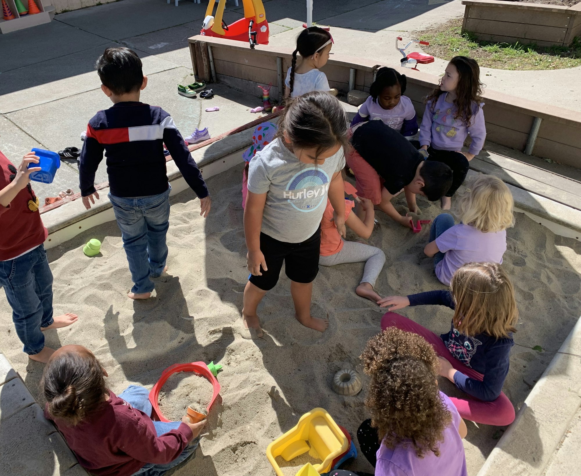 Children playing in a sandbox with toys.