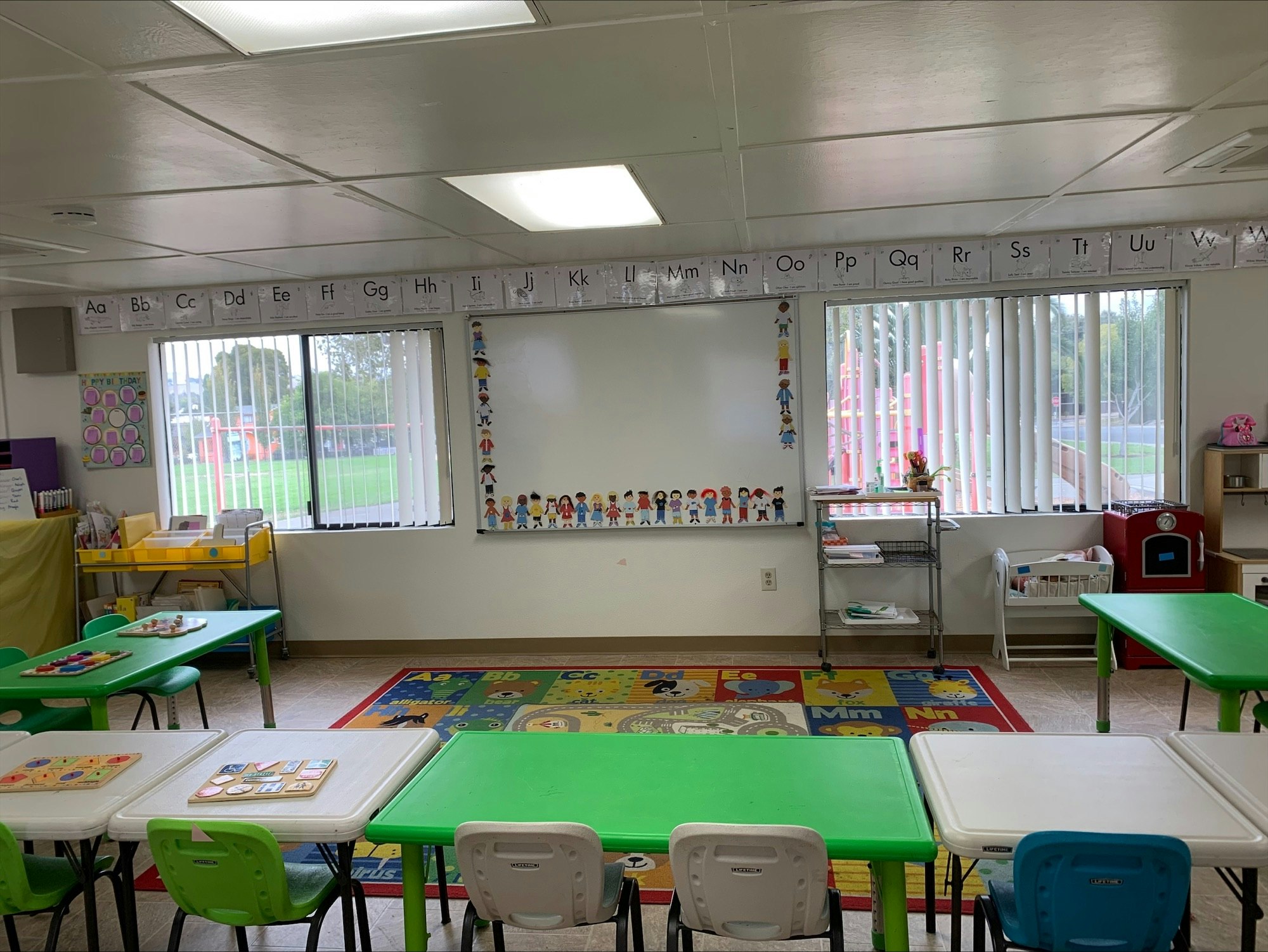 Bright classroom with tables, chairs, educational posters, and alphabet border.