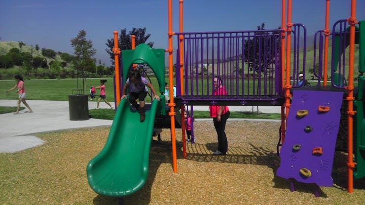 A colorful playground with children playing and an adult supervising.