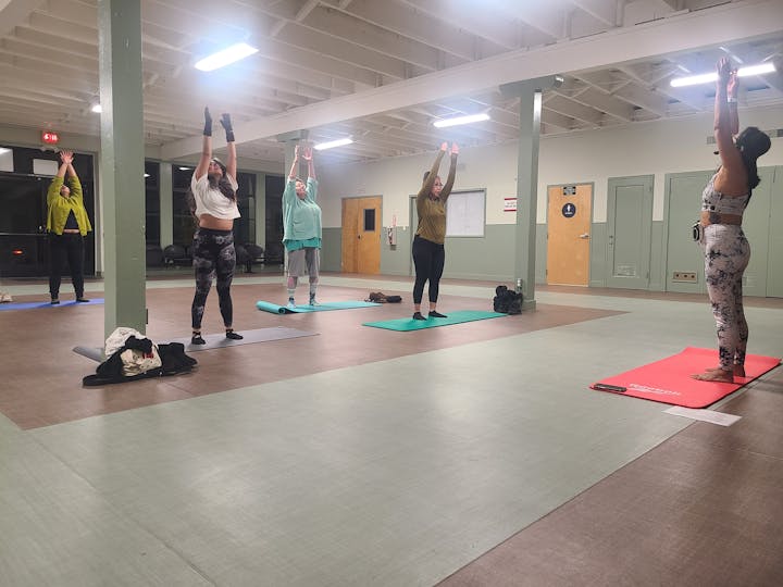 A group of people doing yoga in a studio, standing on mats with arms raised.