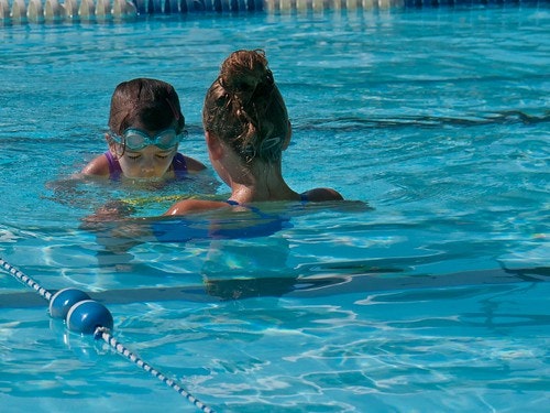 A child wearing goggles and an adult are swimming in a pool.