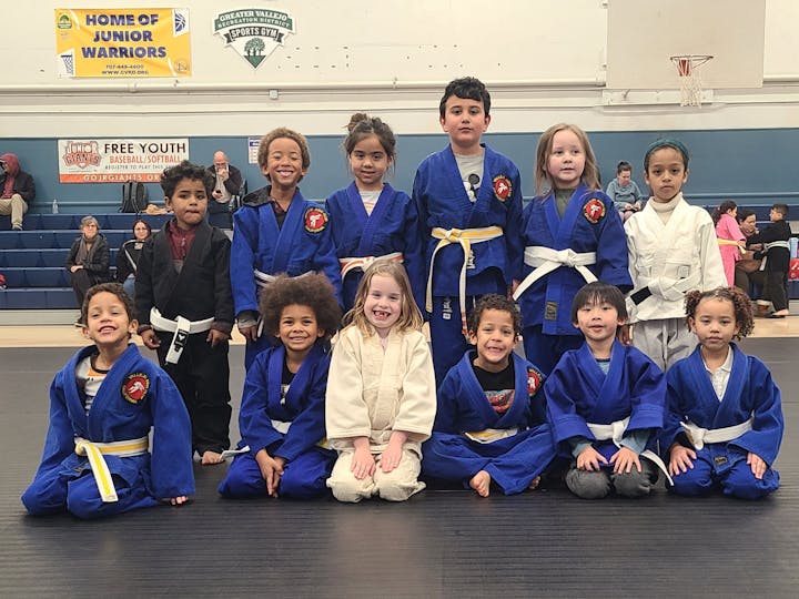 A group of kids in martial arts uniforms posing in a gymnasium setting.