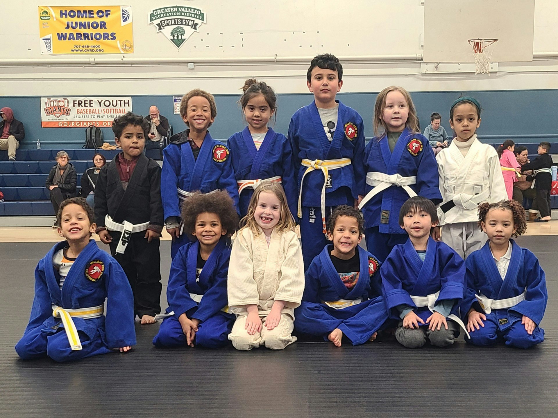 A group of kids in martial arts uniforms posing in a gymnasium setting.