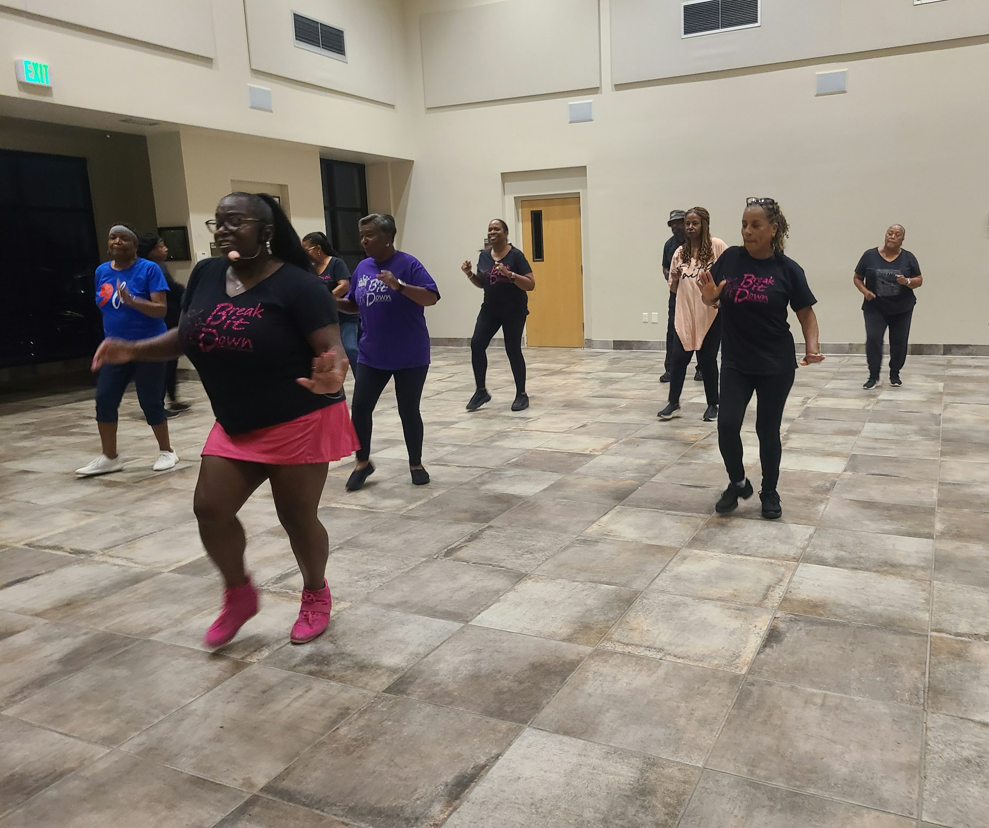 A group of people dancing in a room, wearing casual attire, some in shirts with “Break It Down” printed on them.