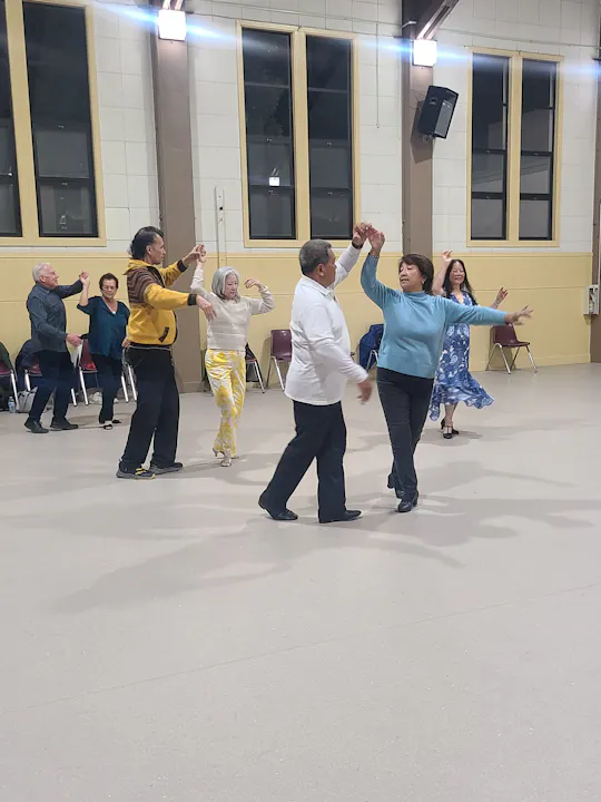 People dancing indoors in a group, with some sitting and watching.