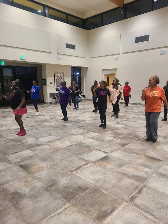 A group of people dancing in a spacious room with tiled floors and high ceilings.