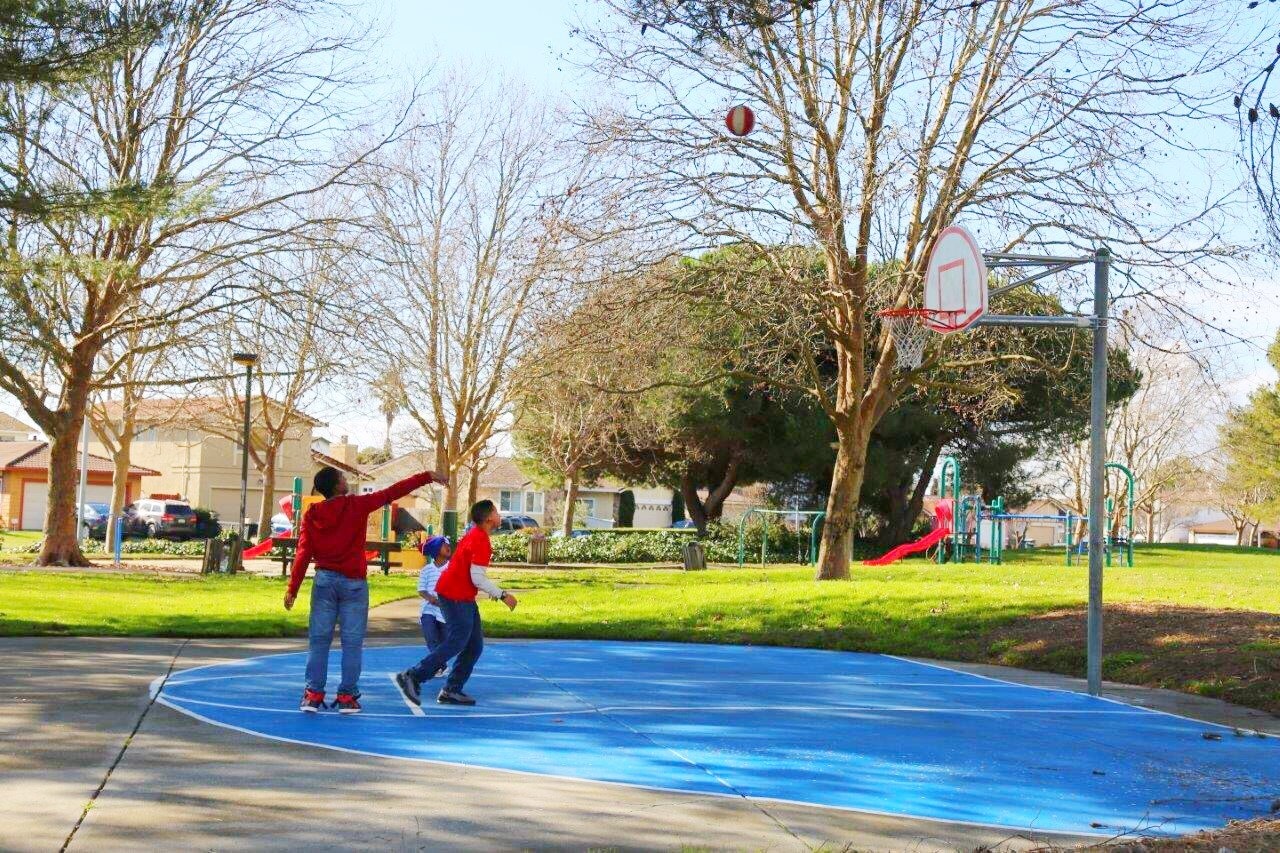 Two people playing basketball on an outdoor court with a ball in the air.