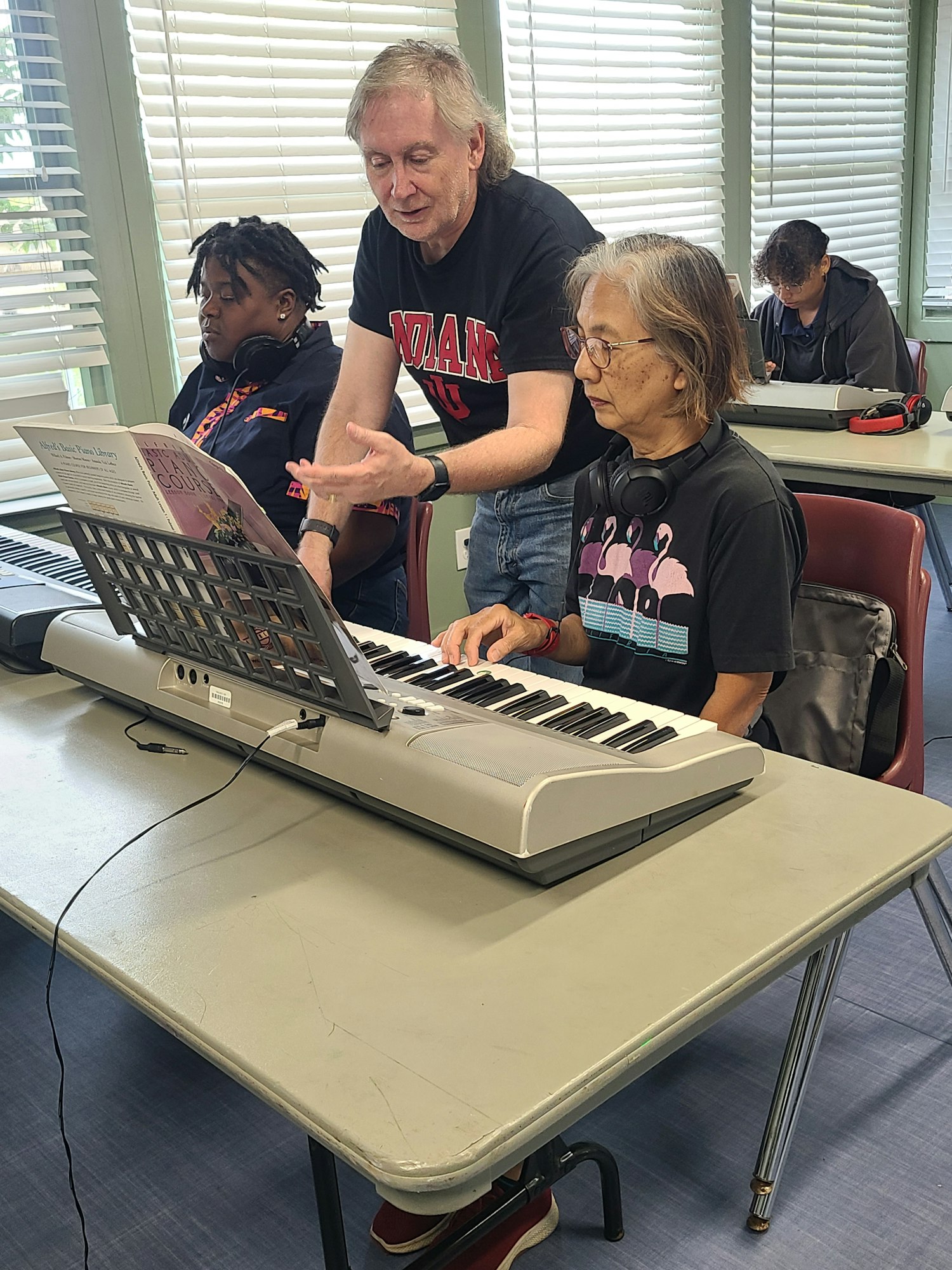A group learning music at a keyboard with a book, one person instructing another.