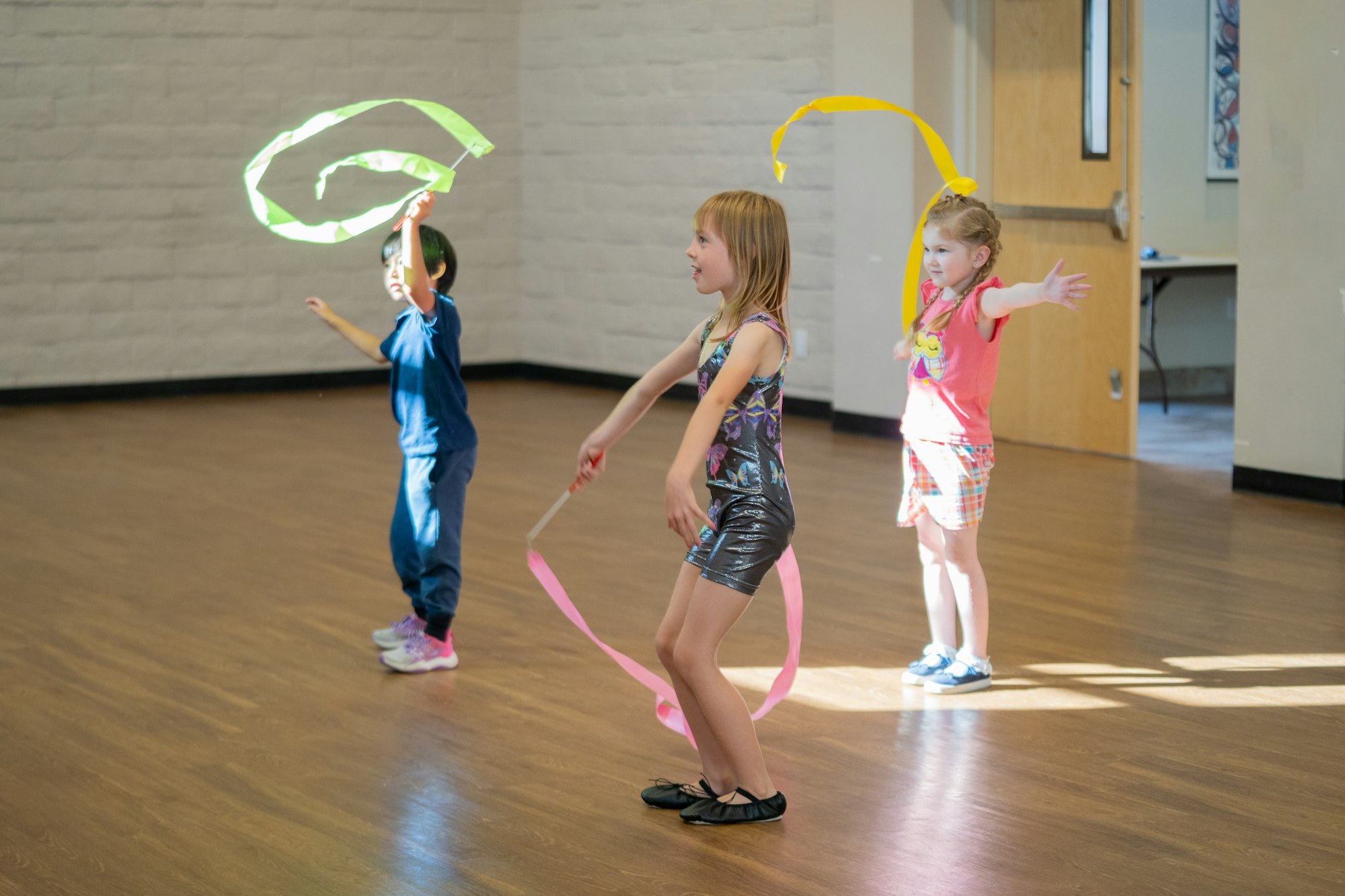 Three children dancing with colorful ribbons in a sunny room.