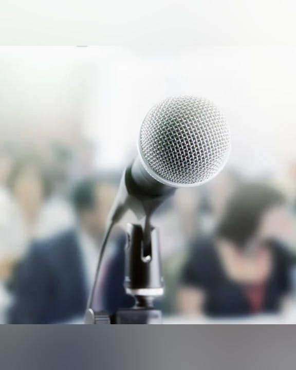 A microphone on a stand in focus with a blurred audience in the background.
