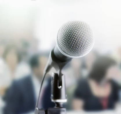 A microphone on a stand in focus with a blurred audience in the background.
