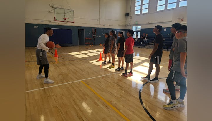 A coach instructing a group of young basketball players in a gymnasium.