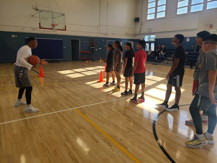 A coach instructing a group of young basketball players in a gymnasium.