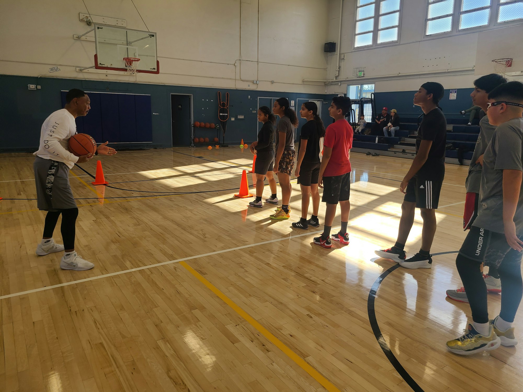 A coach instructing a group of young basketball players in a gymnasium.