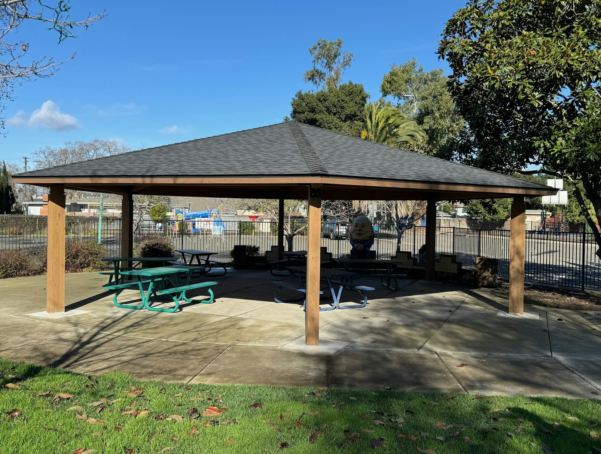 A park gazebo with picnic tables and a playground in the background.