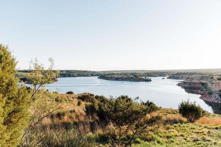 A scenic view of a calm lake surrounded by greenery, with distant hills under a clear sky. Tranquil natural landscape.