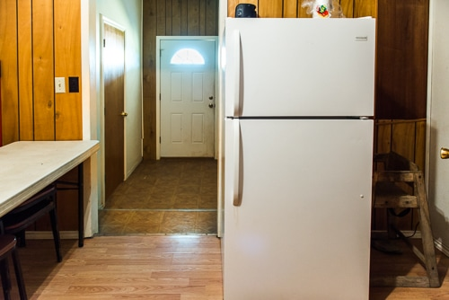 A kitchen area featuring a white refrigerator, a table with chairs, and a door leading to another room.