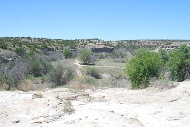 A dry, rocky landscape featuring sparse vegetation, dirt paths, and rolling hills under a clear blue sky.