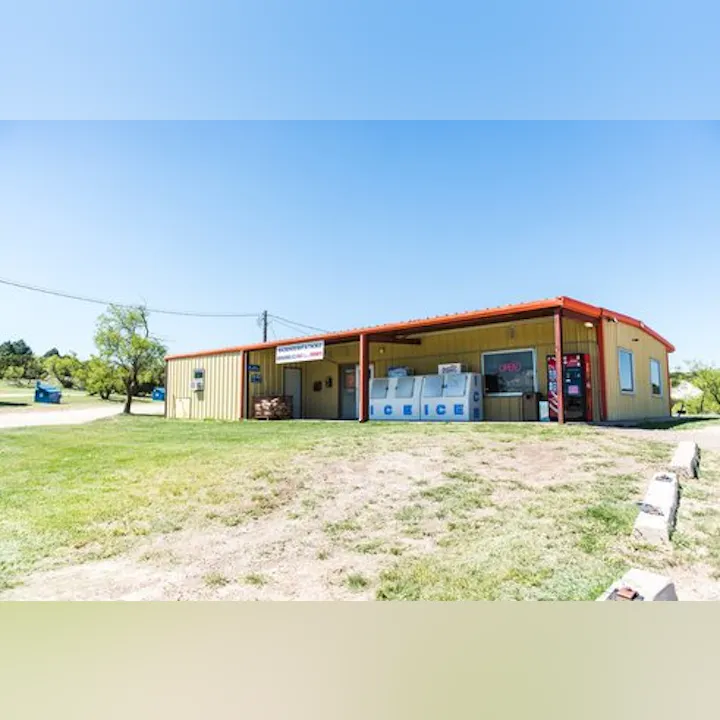 A yellow building with a red roof, signage for "ICE," and a grassy area in front. Clear blue sky in the background.