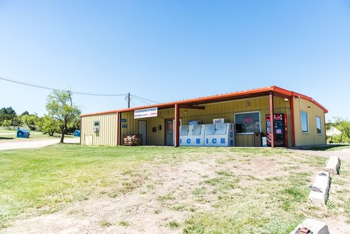 A yellow building with a red roof, signage for "ICE," and a grassy area in front. Clear blue sky in the background.