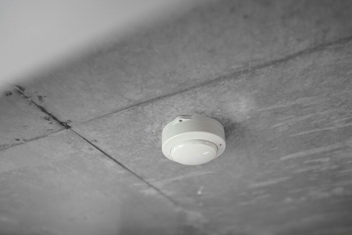 A smoke detector on a ceiling with visible cracks or dirty lines.