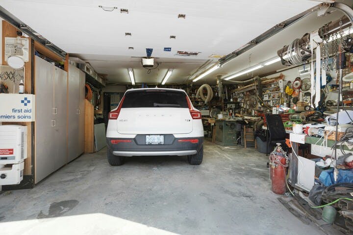 A car parked inside a cluttered garage with various tools and items on shelves.