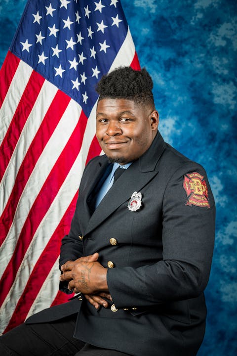 A person in uniform, sitting in front of an American flag.