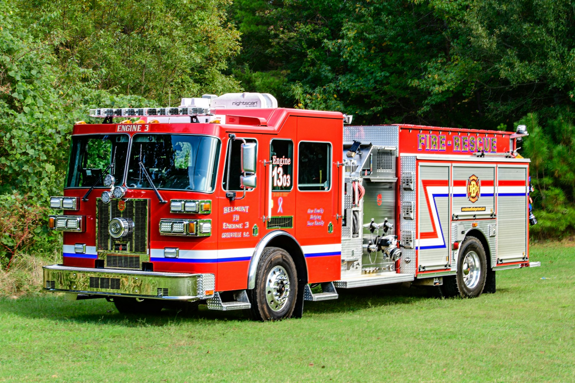 Red fire rescue truck labeled "Engine 3", parked on grass with trees in the background.