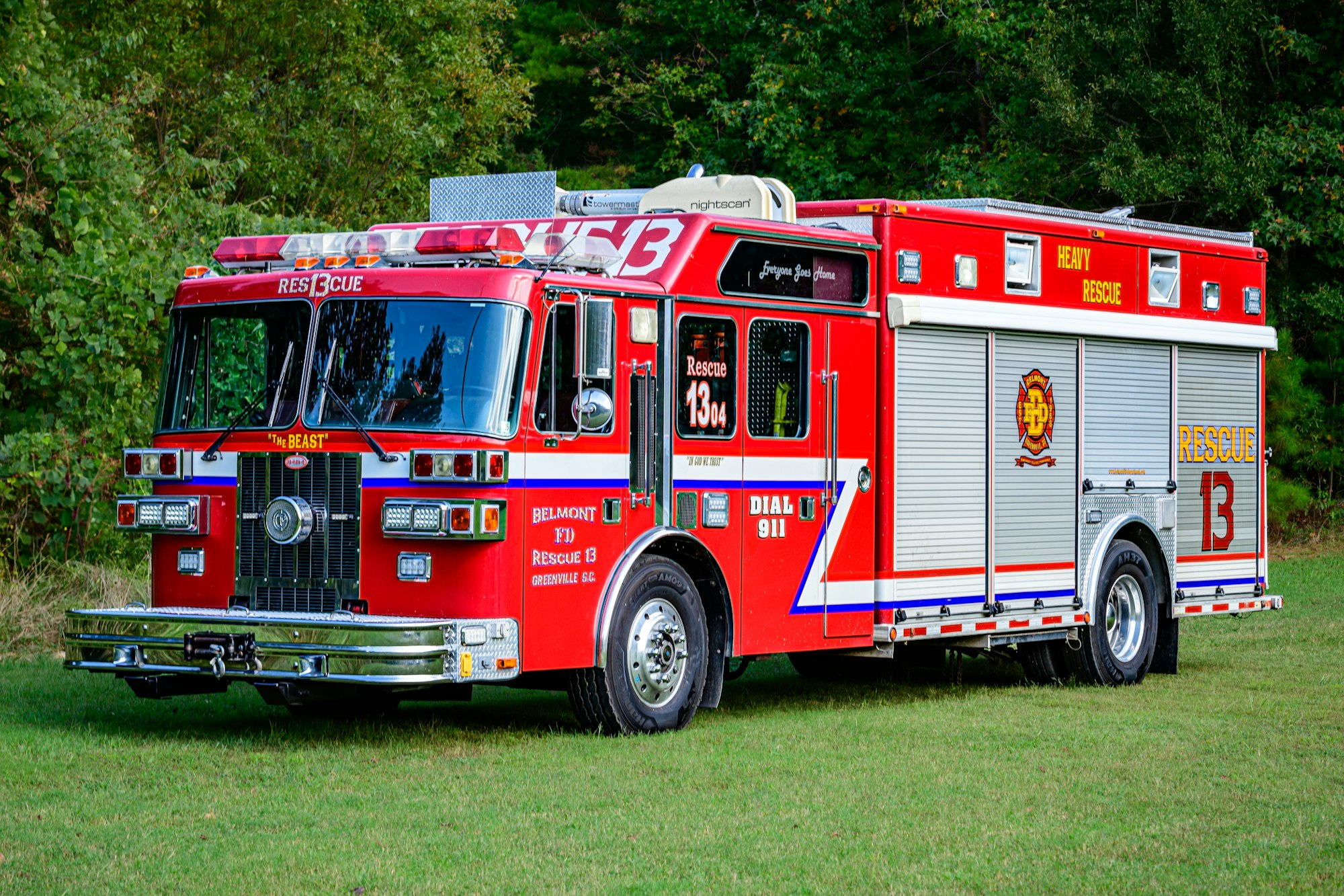 A red fire rescue truck labeled "Rescue 13" parked on grass near trees.