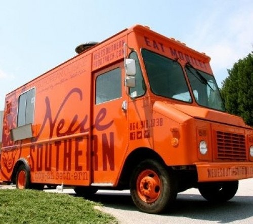 A bright orange food truck parked on the side of the road.