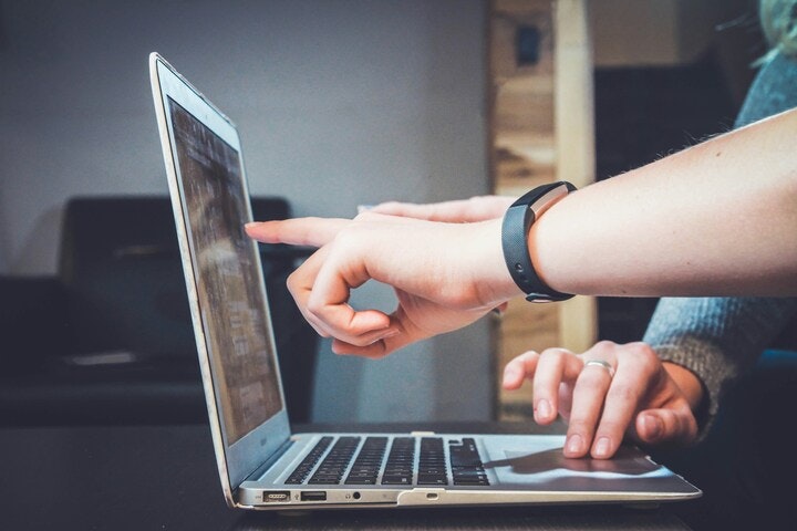 A person pointing at a laptop screen, wearing a fitness band, with a blurred background.