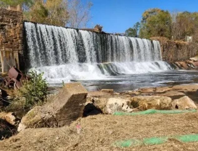 A wide cascade waterfall with a clear blue sky and some greenery in the foreground.