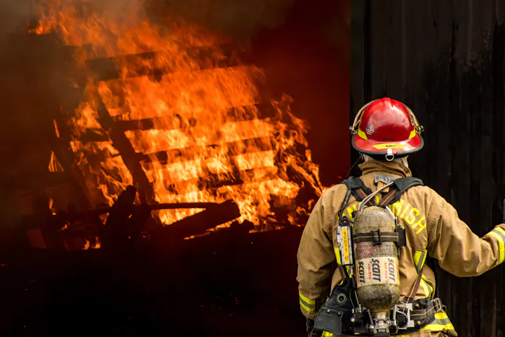 A firefighter stands near a blazing fire, ready to tackle the flames and prevent further damage.