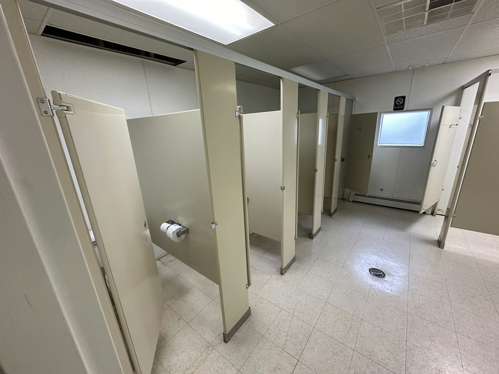 Public restroom interior with stalls, a toilet paper roll, and tiled flooring.