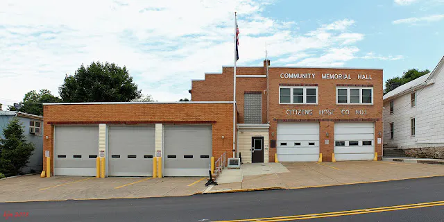 A brick building featuring "Community Memorial Hall" and "Citizens Hose Co. No. 1," with several garage doors and a flag.