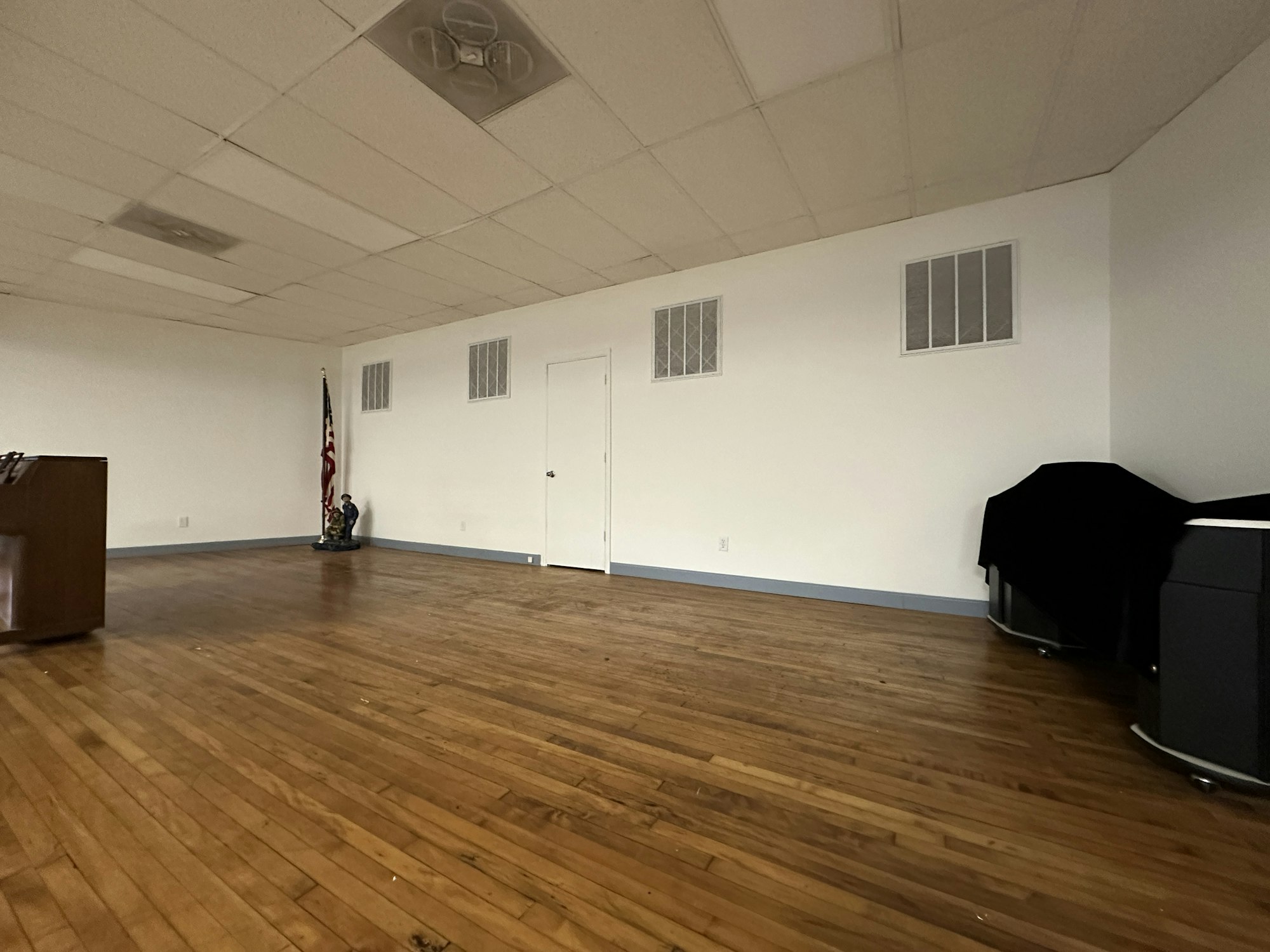An empty room with wooden floors, two doors, an American flag, a podium, and a covered piano.
