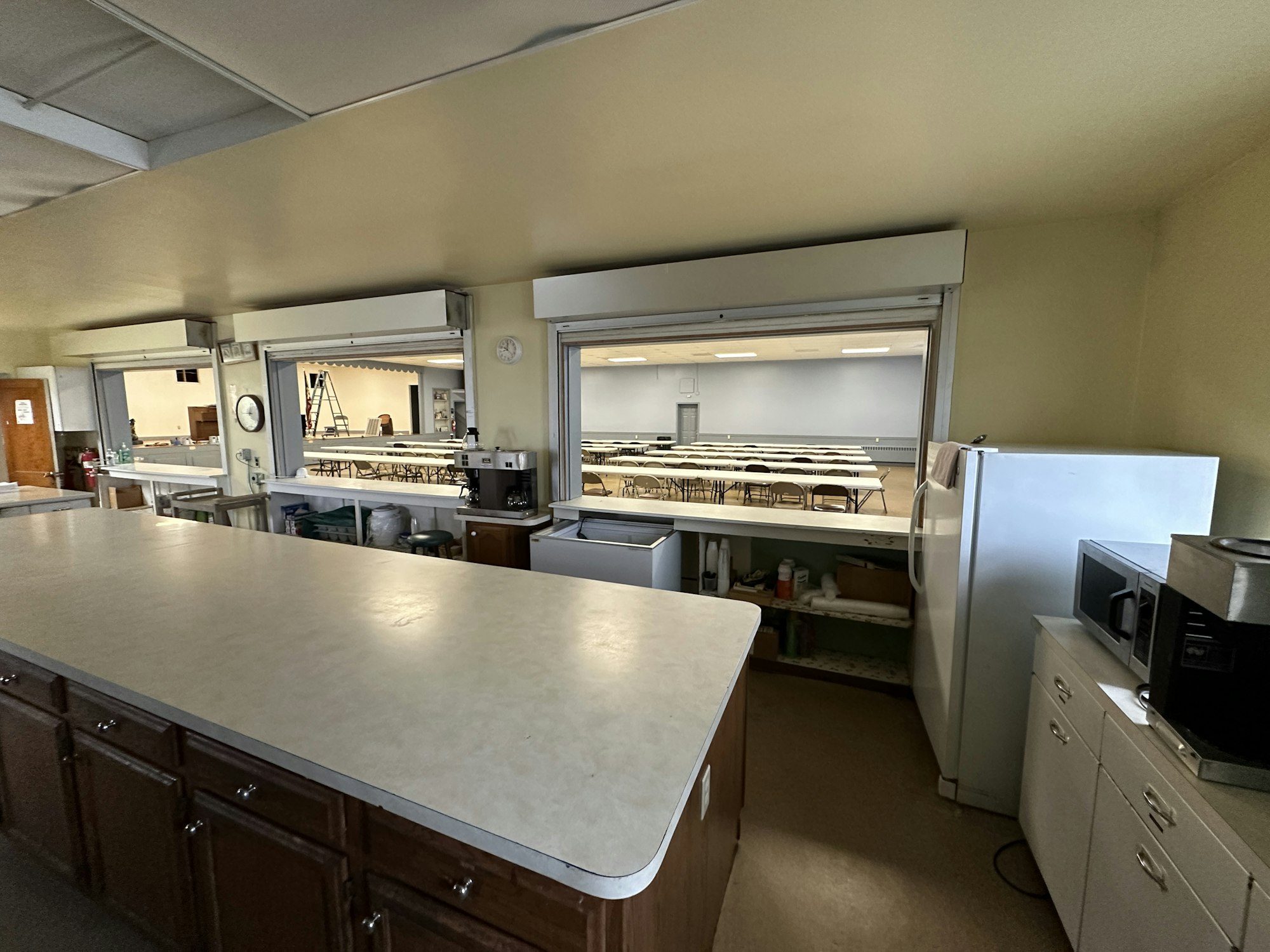 A kitchen area with appliances leading to a cafeteria space with tables and chairs.