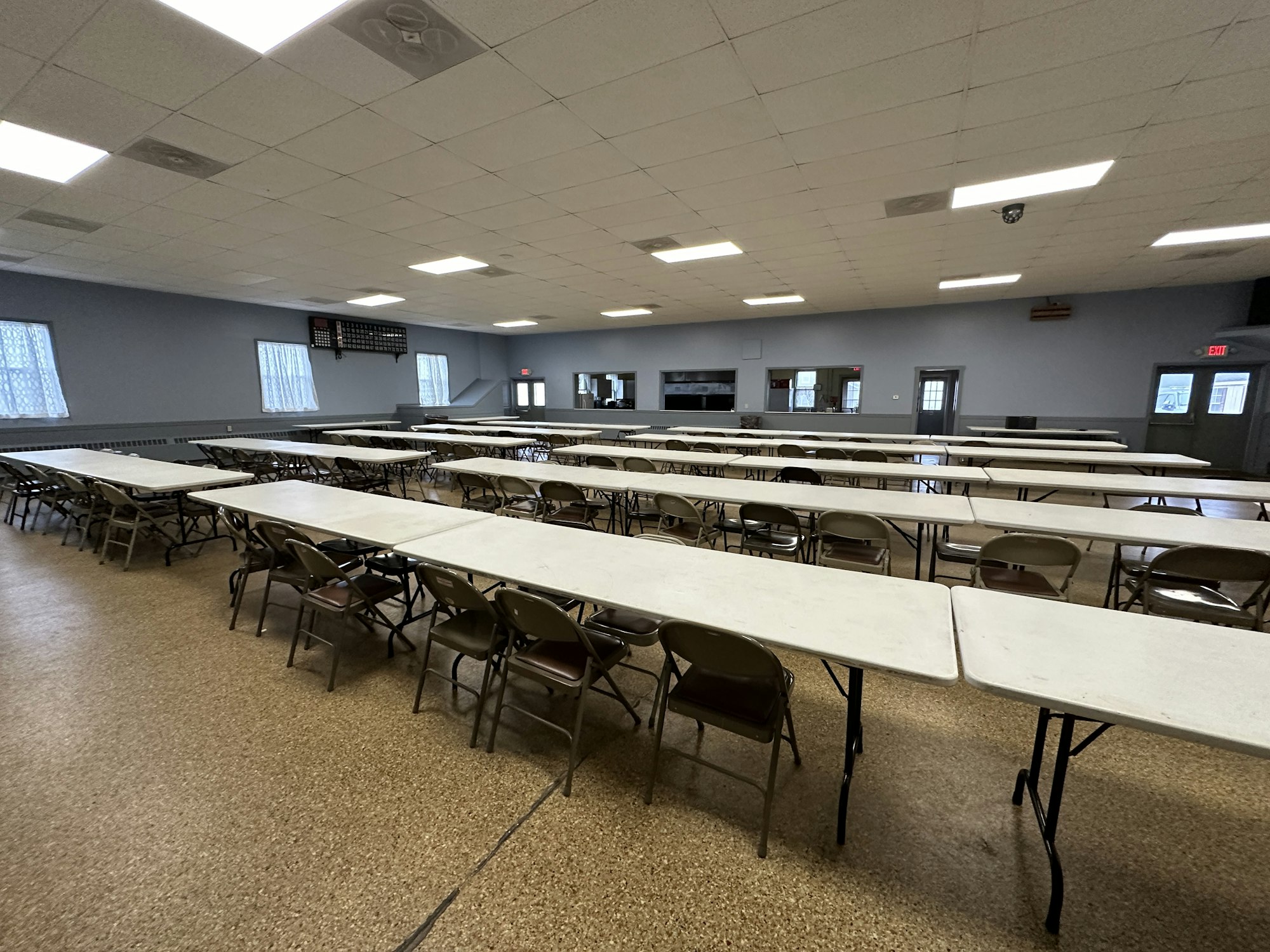 A spacious room with tables, chairs, and a clock on the wall, likely for meetings or events.